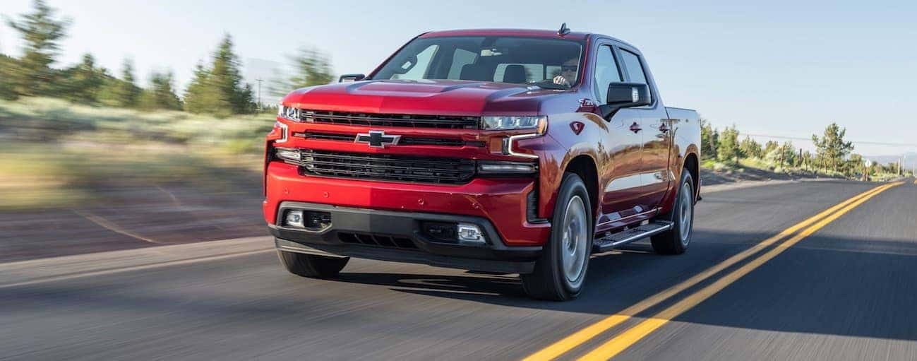 A red 2020 Chevy Silverado 1500 is driving on a tree lined road.
