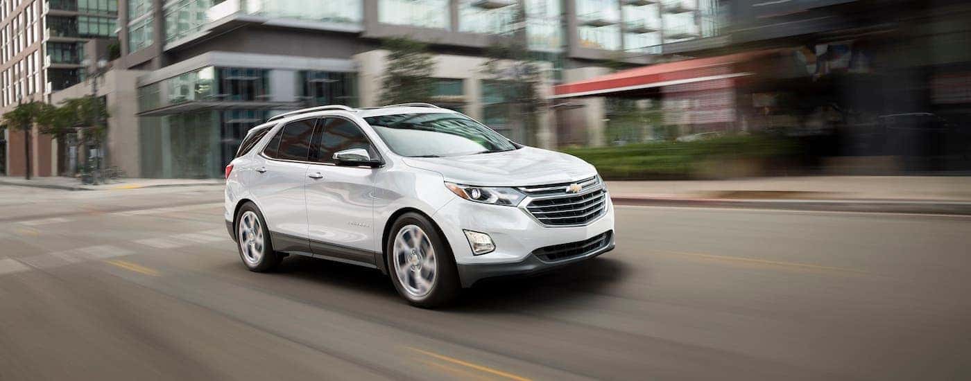 A white 2020 Chevy Equinox is driving on a city street after winning the 2020 Chevy Equinox vs 2020 Hyundai Santa Fe comparison.