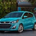 A teal 2021 Chevy Spark is parked in front of a wall of plants.