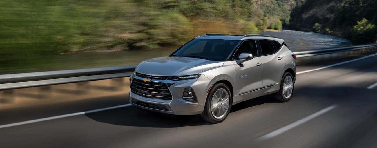 A silver 2021 Chevy Blazer is driving past a guardrail and trees.