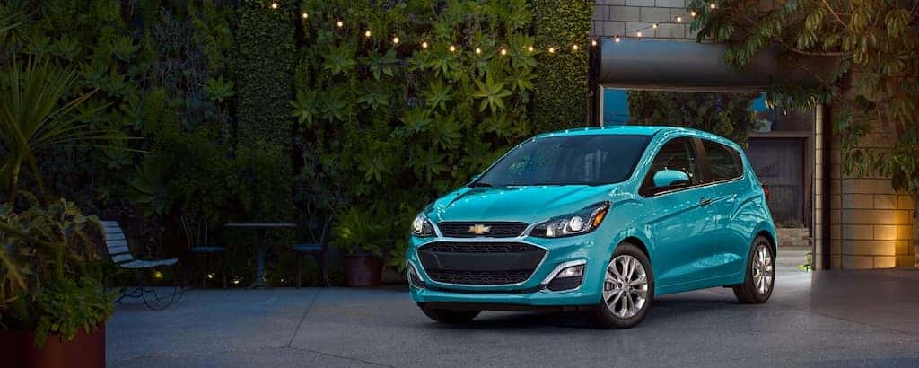 A blue 2021 Chevy Spark is parked in front of a wall of plants.