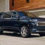 A blue 2021 Chevy Suburban is parked in front of a modern home.