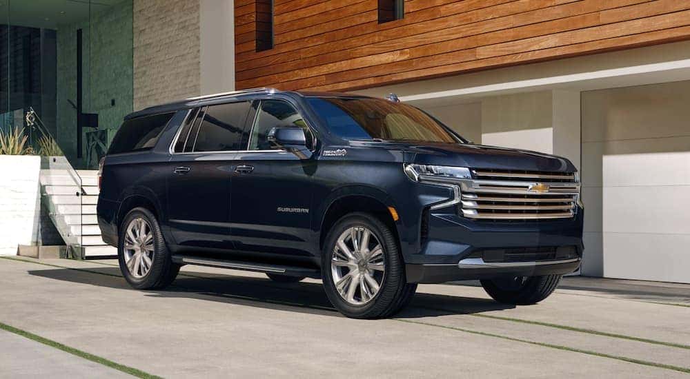 A blue 2021 Chevy Suburban is parked in front of a modern home.