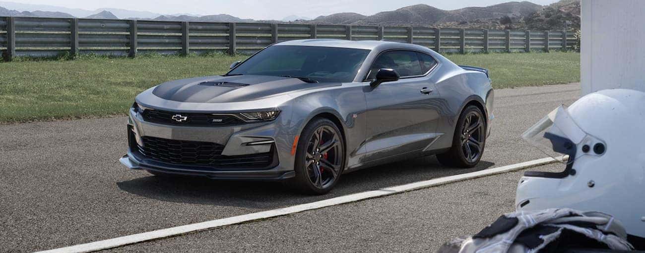 A silver 2021 Chevy Camaro is parked in front of a fence on a racetrack.