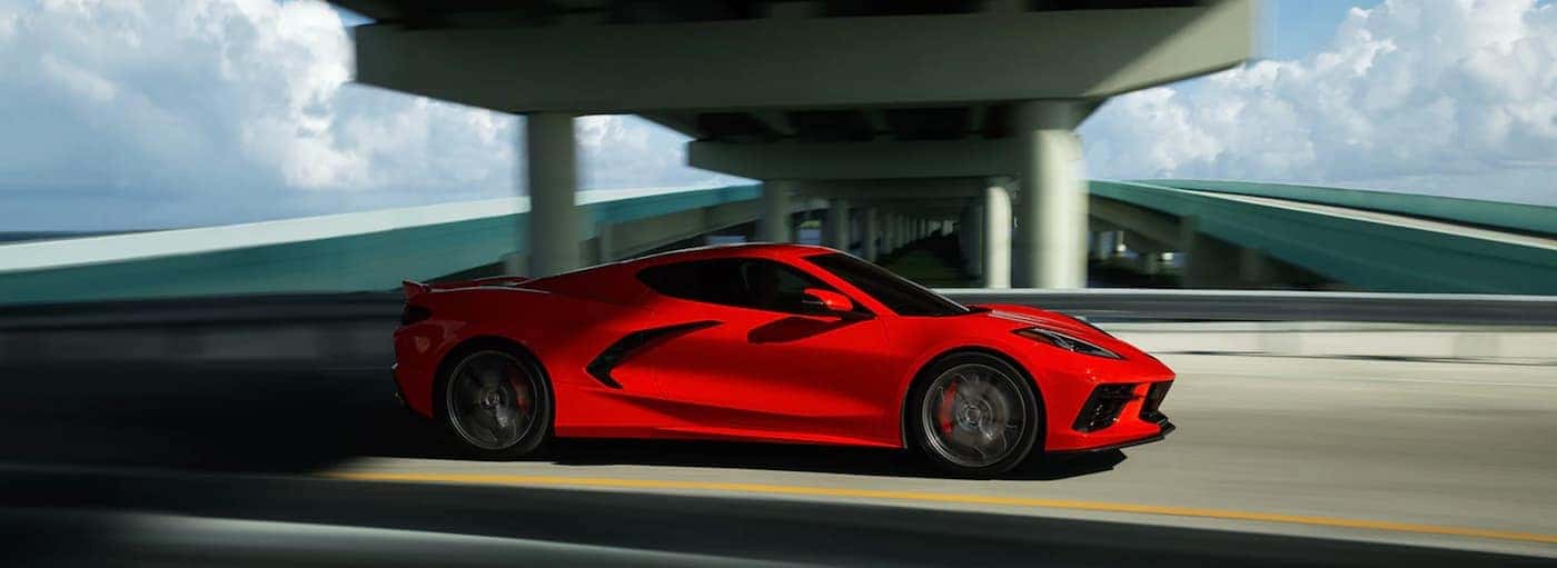 A red 2021 Chevy Corvette Stingray is driving under a highway overpass.