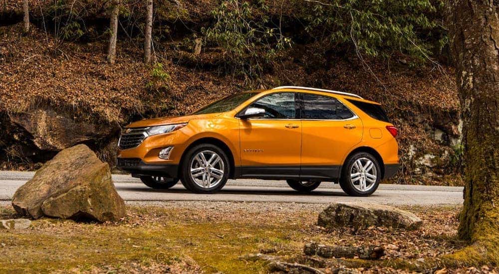 An orange 2017 Chevy Equinox is shown from the side driving on a hill with fall foliage.