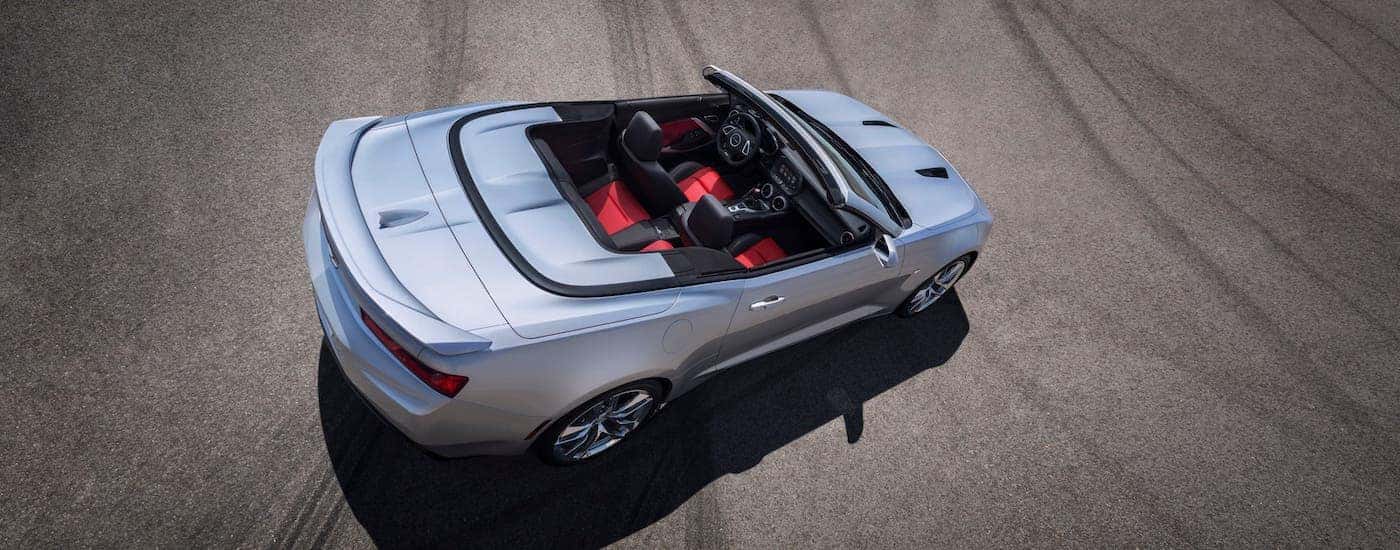 A silver 2021 Chevy Camaro convertible with black and red seats is shown from a high angle in an empty lot.
