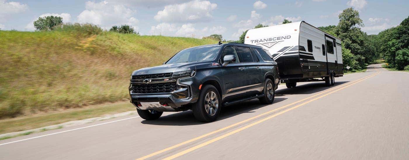 A dark gray 2021 Chevy Suburban Z71 is towing a camper on a highway.