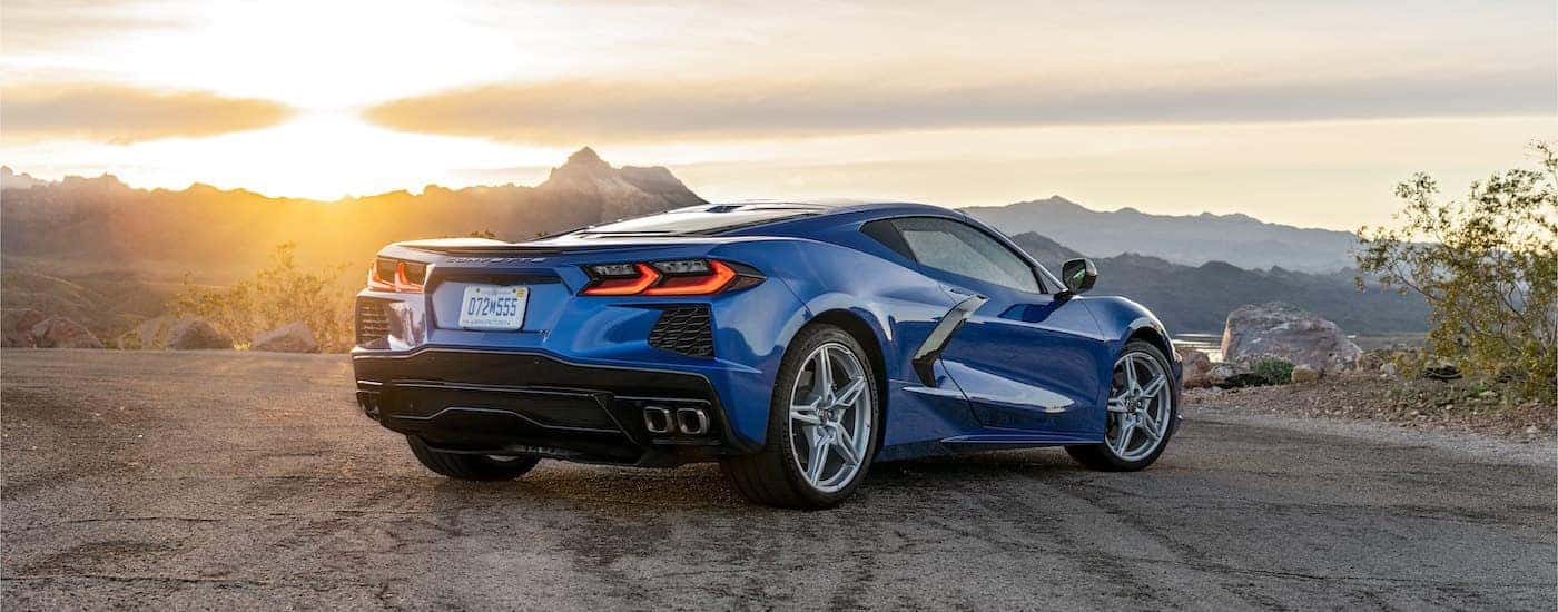 A blue 2022 Chevy Corvette Stingray is shown from behind parked with a sunset in the distance.