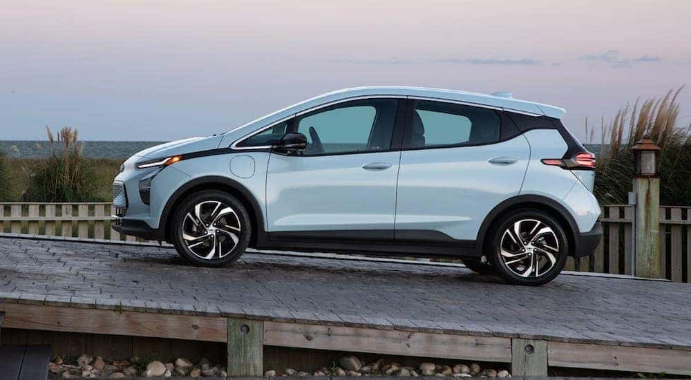 A light blue 2022 Chevy Bolt is driving up a ramp by the beach.