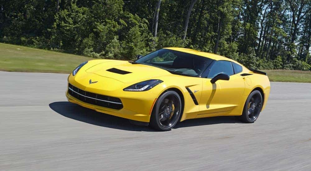 A yellow 2014 Chevy Corvette is shown driving down an empty road.