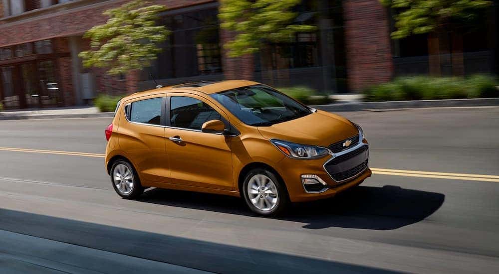 An orange 2020 Chevy Spark is shown driving on a city street.