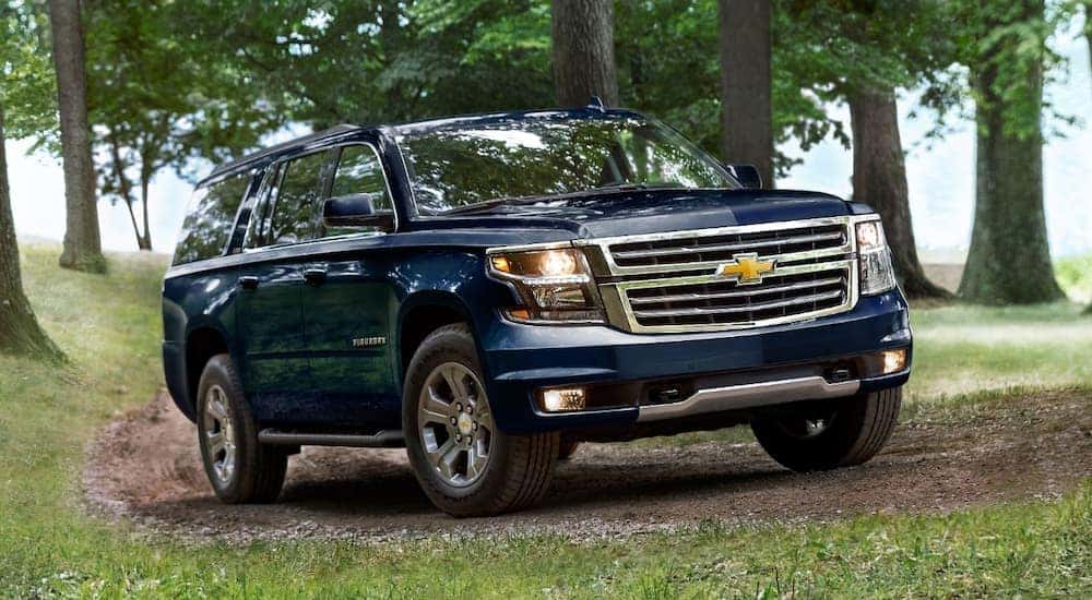 A blue 2020 Chevy Suburban is shown driving on a dirt trail after leaving a certified pre-owned Chevrolet dealer.