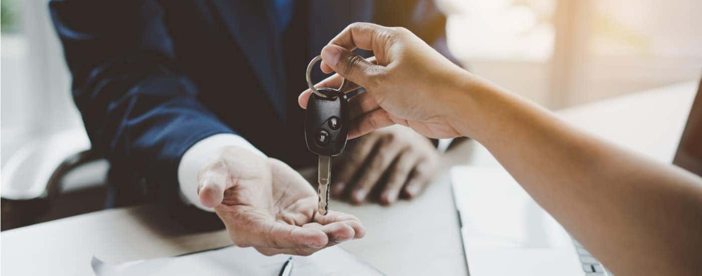 A customer is shown handing a car salesman a carkey.