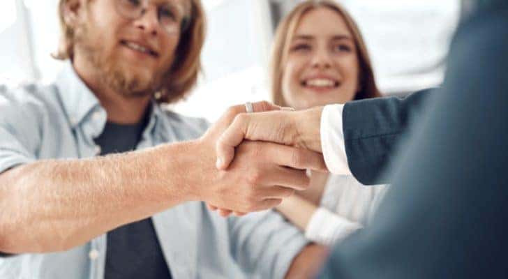 A couple is shown shaking hands with a car salesman.
