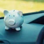 A white piggy bank is shown on the dashboard of a vehicle.