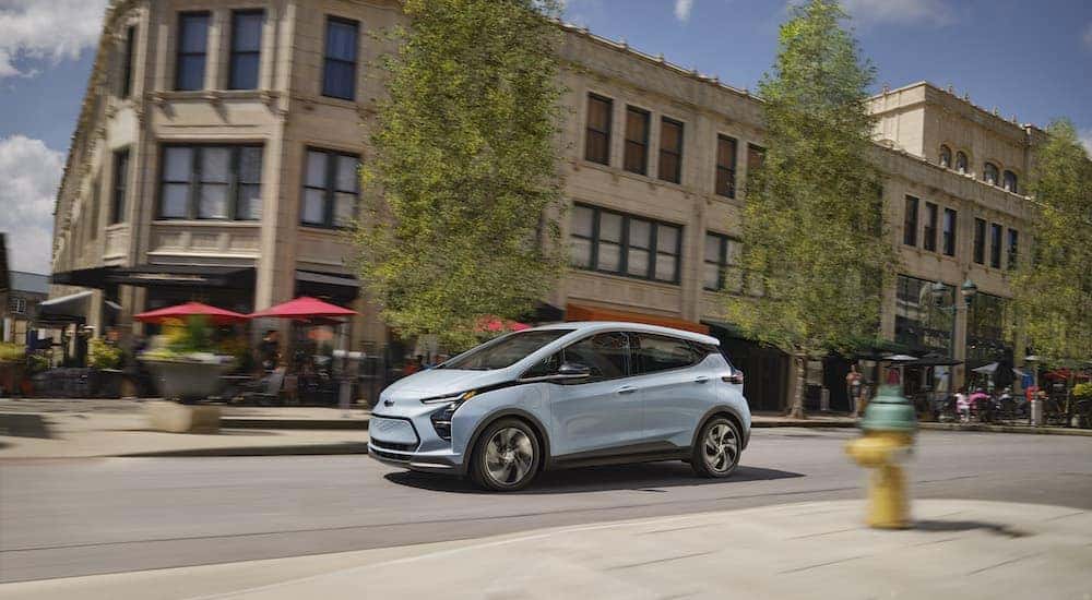 A blue 2023 Chevy Bolt EV is shown from the side while driving on a city street.