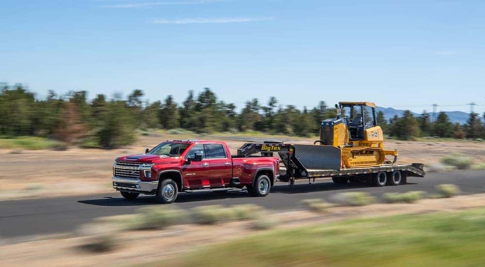 A red 2022 Chevy Silverado 3500 HD is shown from the side while towing a bulldozer after leaving a dealer that had a used Chevy Silverado for sale..