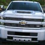 A white 2017 Chevy Silverado is parked on a road with trees in the background.