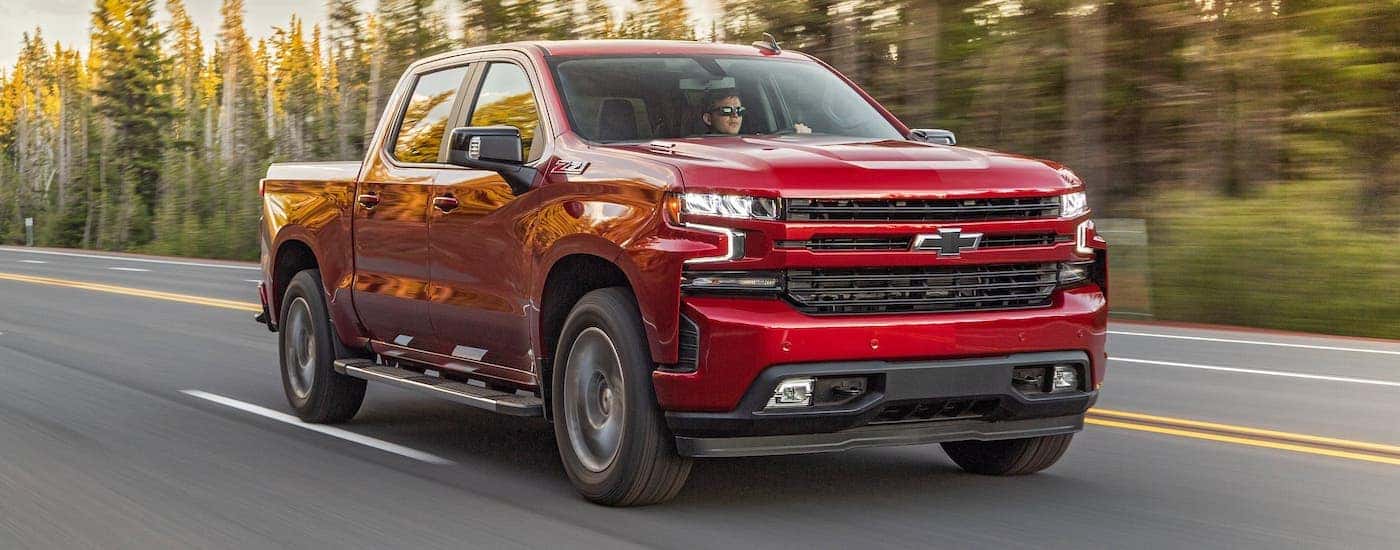 A red 2020 Chevy Silverado is driving on a tree-lined highway.