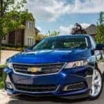 A blue 2016 Chevy Impala is parked in front of a house in a neighborhood.
