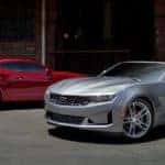 A red 2019 Chevy Camaro is parked next to a grey one outside a brick building.