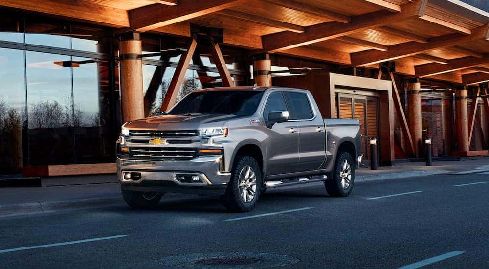 A grey 2019 Chevy Silverado 1500 is parked outside a wood and glass building.