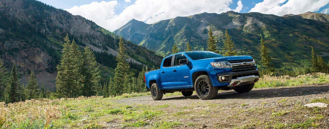 A blue 2022 Chevy Colorado is shown from the side parked in a field in front of a mountain range.