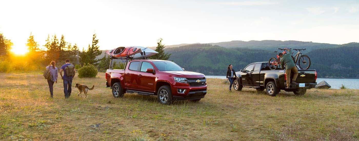 A red and a black 2015 Chevy Colorado are in a field with kayaks and bikes.