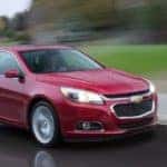 A red 2015 Chevy Malibu is driving in the rain.