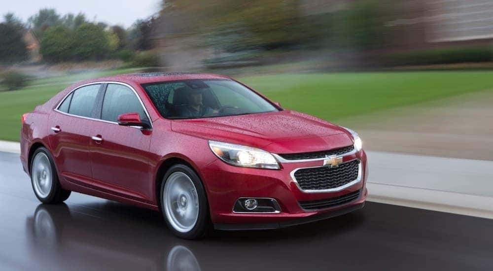 A red 2015 Chevy Malibu is driving in the rain.