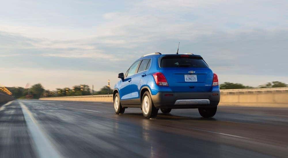 A blue 2015 Chevy Trax is driving on a sunny highway.