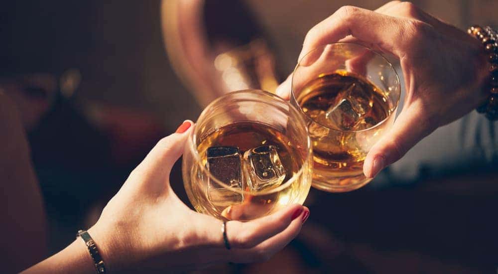 A couple's hands are holding whiskey glasses at an Atlanta, GA event.