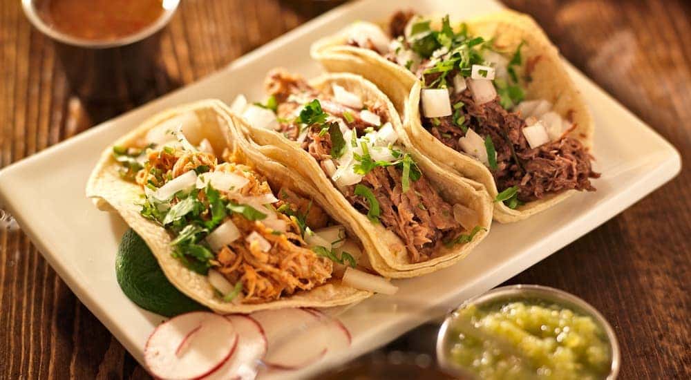 A plate of chicken tacos are on a wooden table.