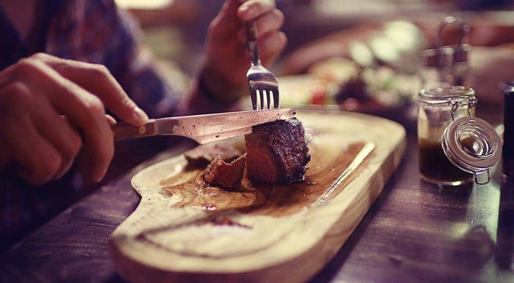 A man is cutting a steak on a wooded board.