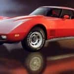 A red 1977 Chevy Corvette is on a reflective showroom floor.