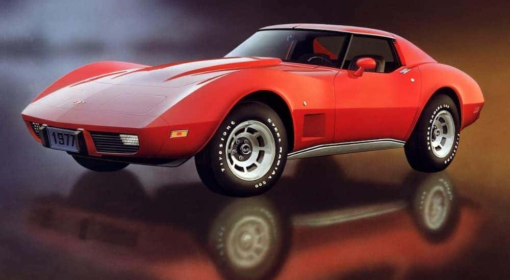 A red 1977 Chevy Corvette is on a reflective showroom floor.