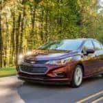 A red 2016 used Chevy Cruze, which is a popular used Chevrolet model, is driving on a treelined road near Buford, GA.