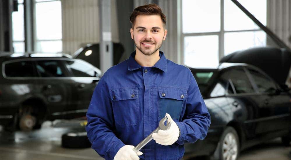 A smiling mechanic is holding a wrench.