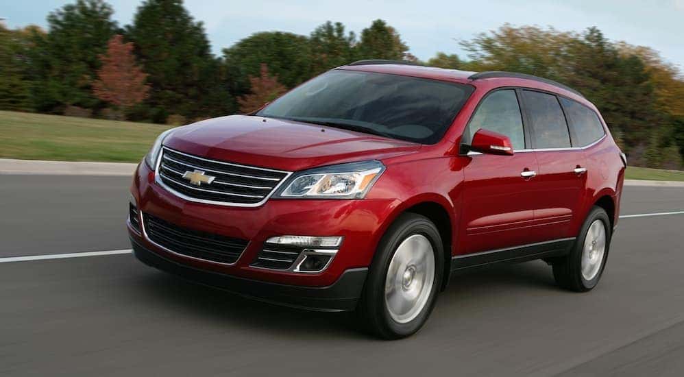 A red 2015 Chevy Traverse is driving on a treelined road.
