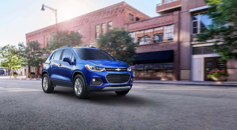 A blue 2017 Chevy Trax is driving past blurry buildings on a city street.