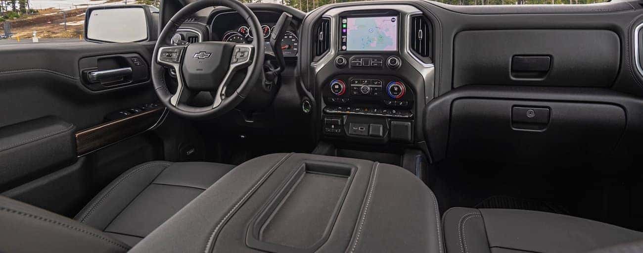 The front black leather interior of the 2020 chevy Silverado 1500 is shown with an infotainment system and driver's display.