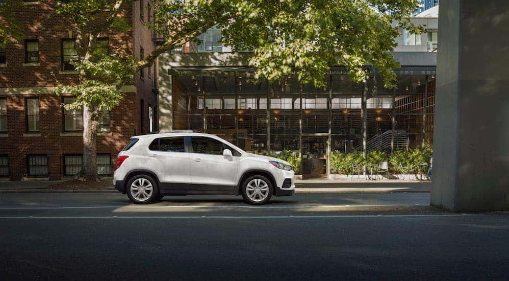 A white 2020 Chevy Trax is parked on the side of a city street next to trees.