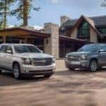 Two popular Chevy SUVs, a grey 2020 Suburban and a silver 2020 Tahoe, are parked in front of a large home.