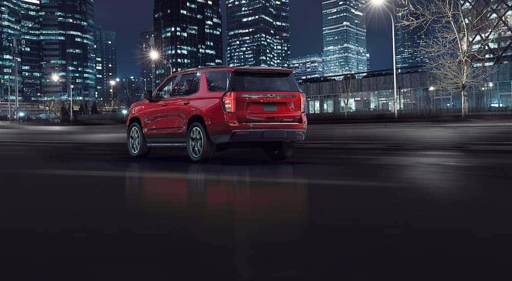 A red 2021 Chevy Tahoe, which is soon to be a popular option among Chevy SUVs, is driving on a highway past lit up city buildings near Buford, GA.