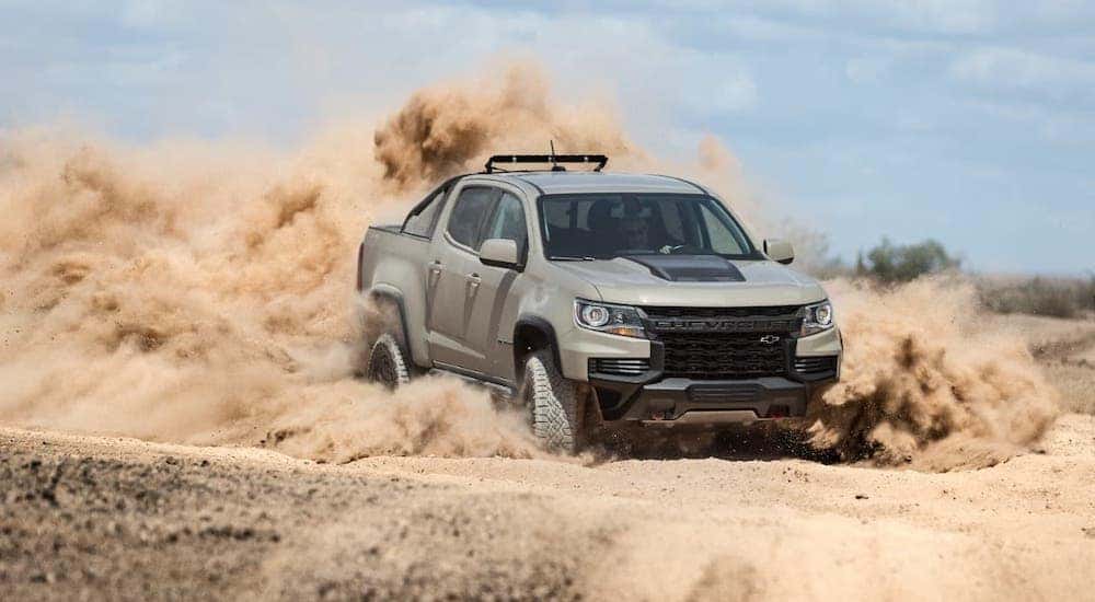 A tan 2021 Chevy Colorado ZR2 is kicking up dirt on a track after leaving a Chevy Dealership in Buford, GA.