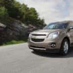 A beige 2015 Chevy Equinox is driving around a corner with a hill behind it near Buford, GA.
