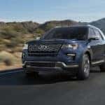 A blue 2018 Ford Explorer is driving past hills with a lake in the distance.