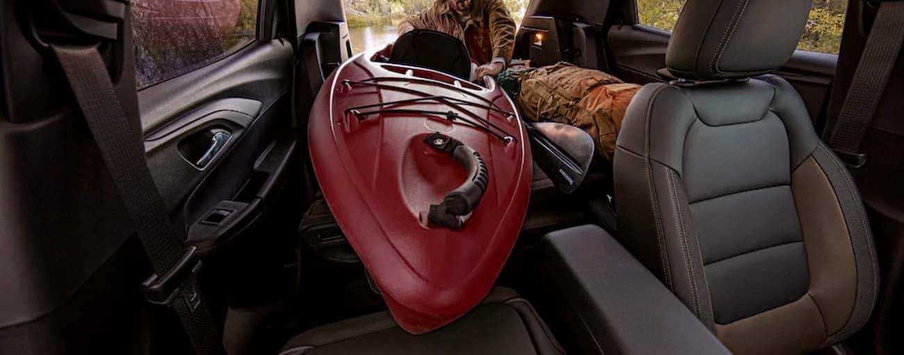 A front to back view of a man sliding a kayak into a 2021 Chevy Trailblazer is shown.
