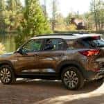 A brown and white 2021 Chevy Trailblazer is driving on a dirt road past a pond.